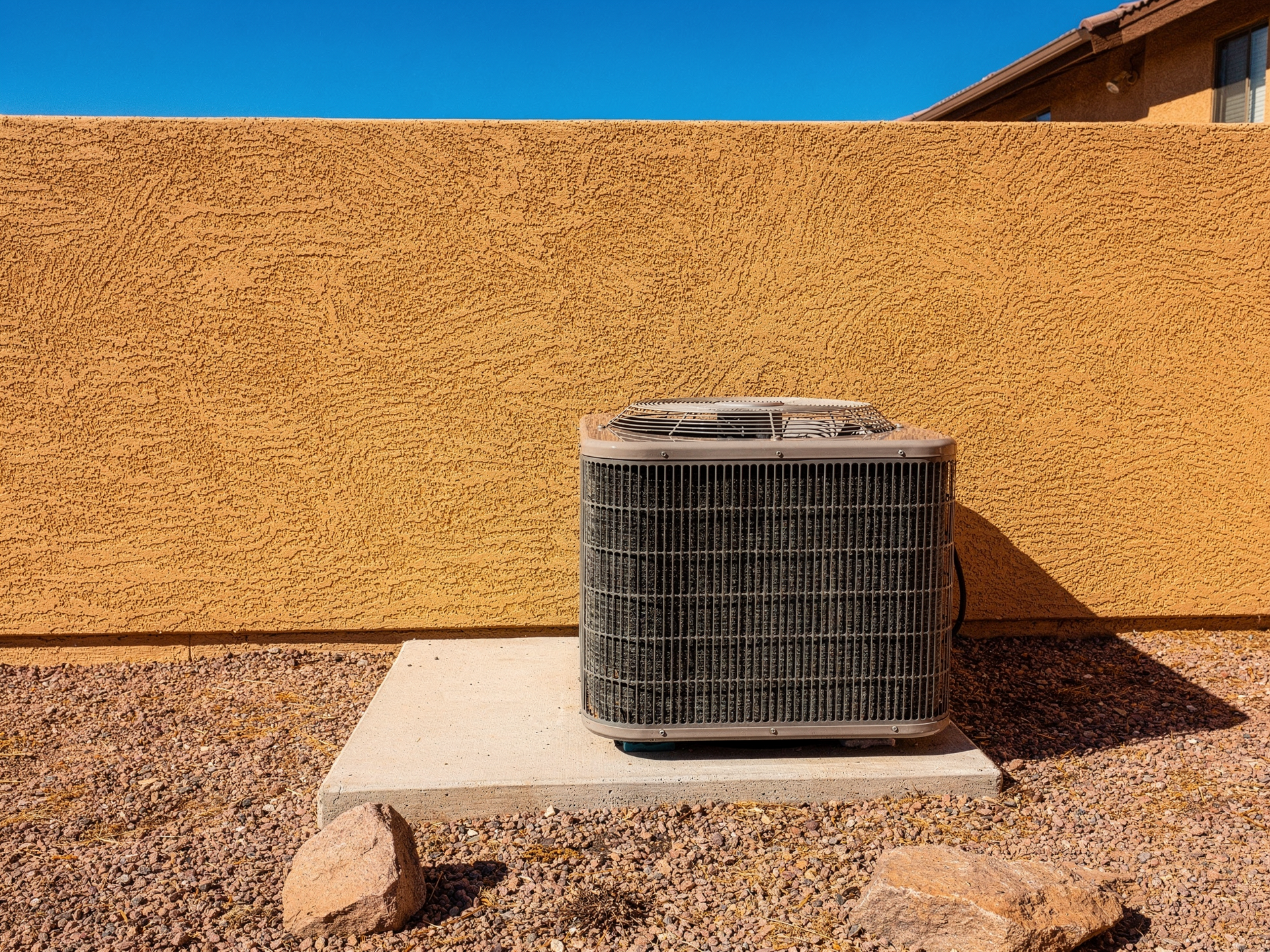 A residential AC condenser unit running outside a Phoenix home under a clear blue desert sky